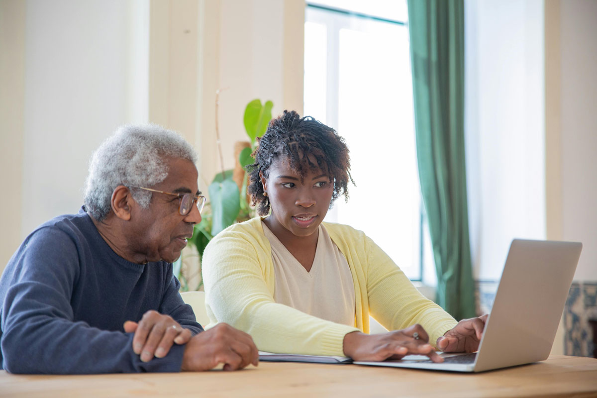 An older man and a younger woman reviewing documents together on a laptop