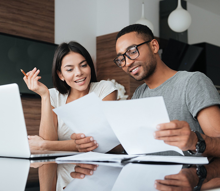A couple smiling as they look over papers together at a table